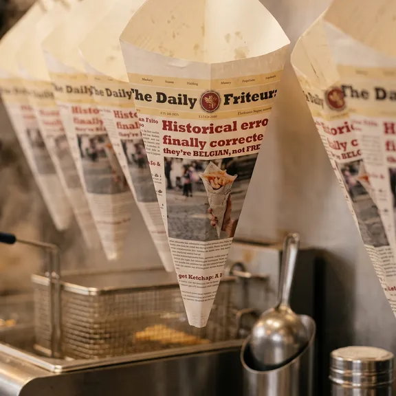 Daily Friteur newspaper cones hanging on hooks above the fryer station