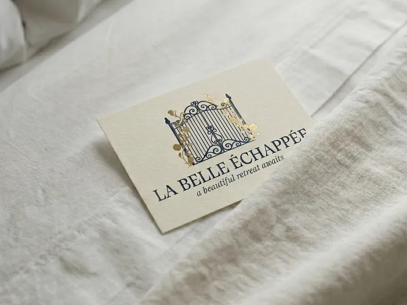 La Belle Échappée gold-foil welcome card on white linen bedding