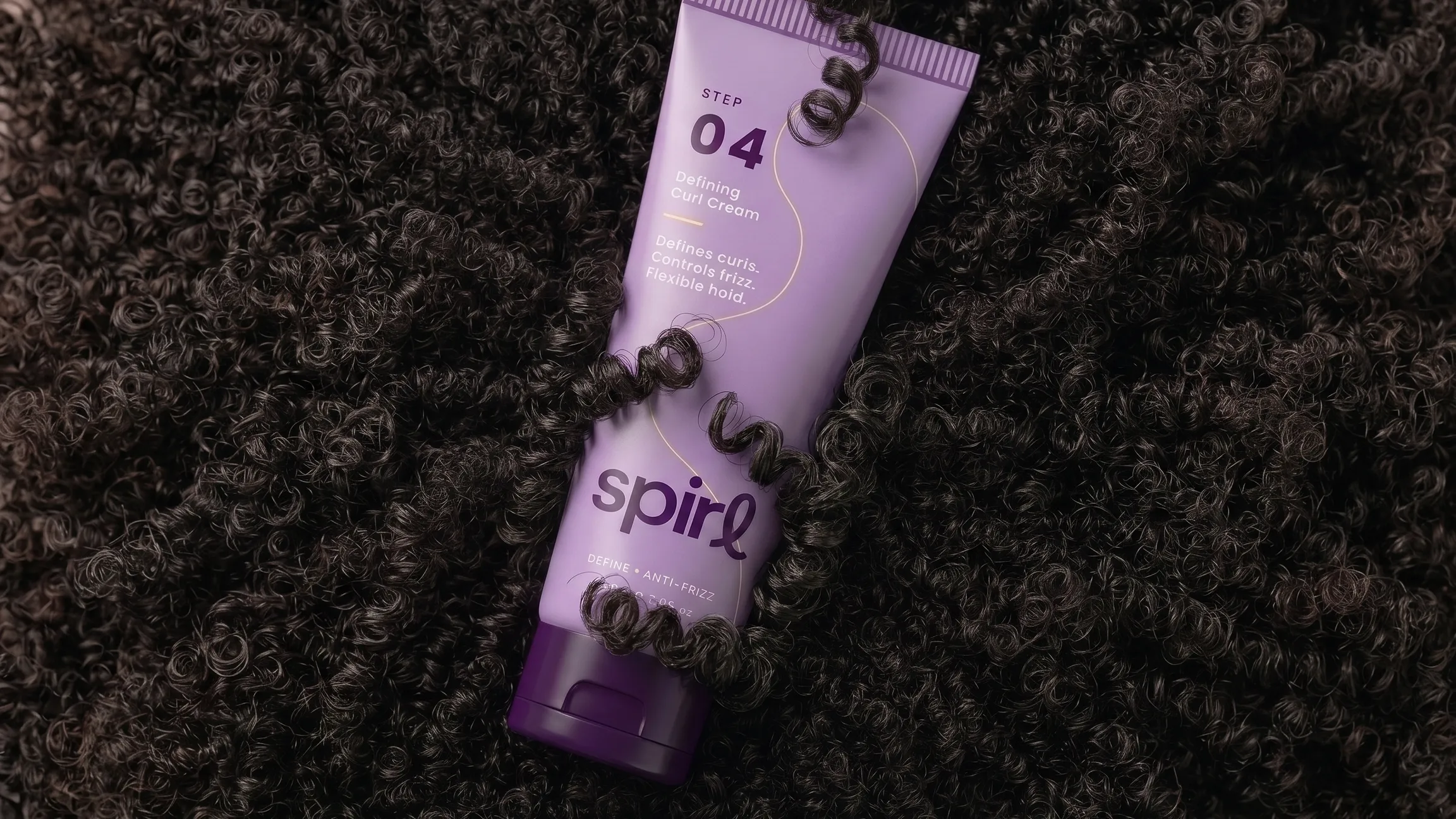 Lilac Spirl Step 04 Defining Curl Cream tube resting on a bed of dark natural curls