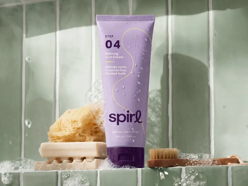 Lilac Spirl Defining Curl Cream tube on a sage-green tiled shower ledge