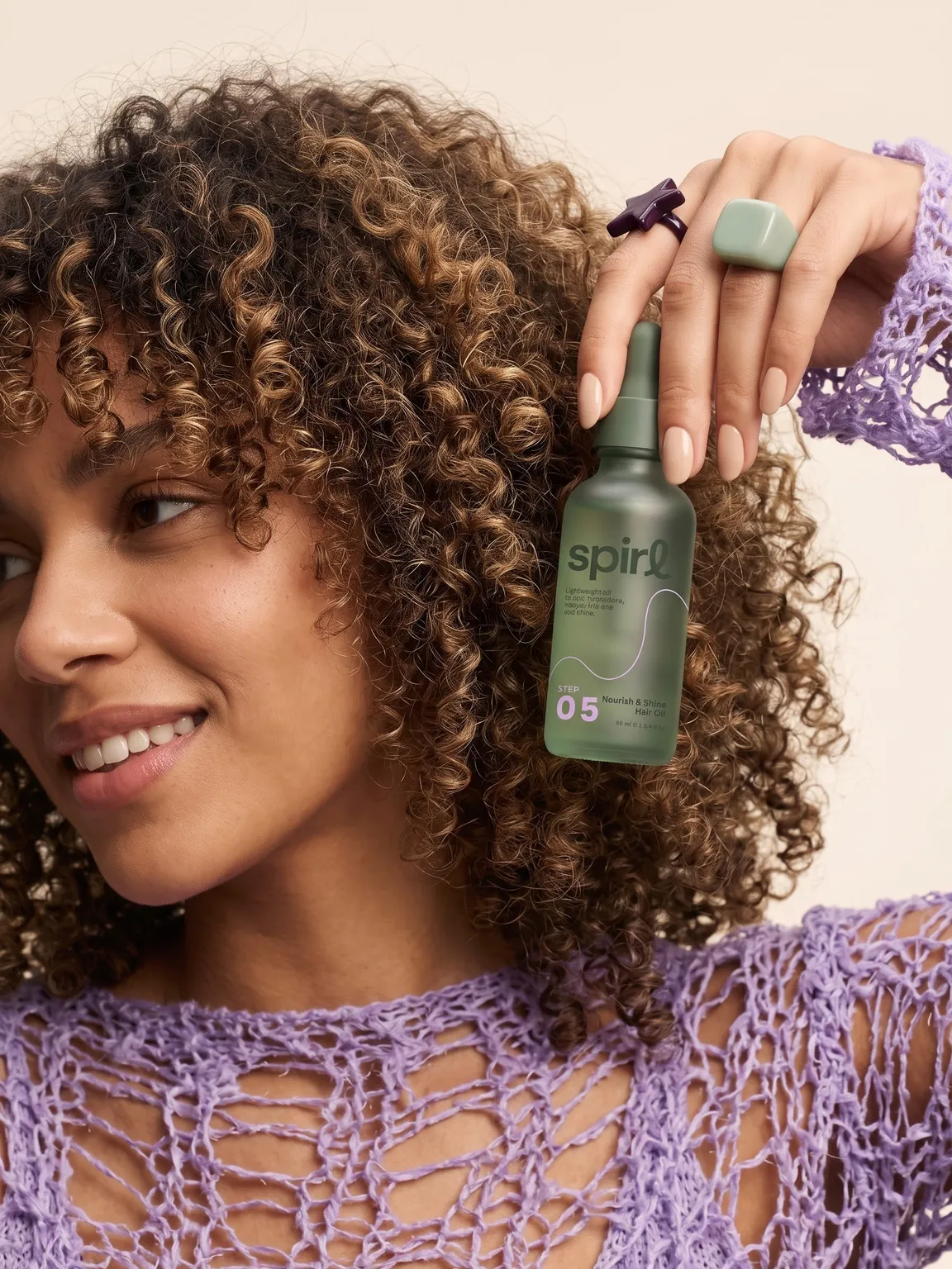 Model with defined curls holding the Step 05 Nourish & Shine Hair Oil beside her face