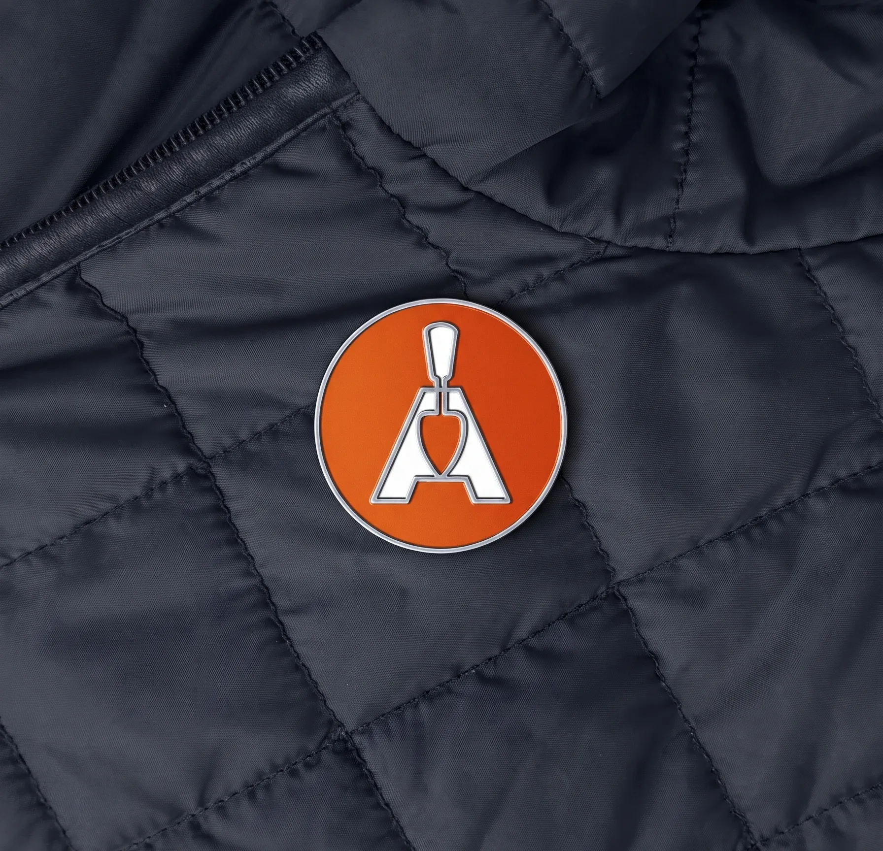 Orange enamel Structa pin badge fastened to a navy quilted work jacket